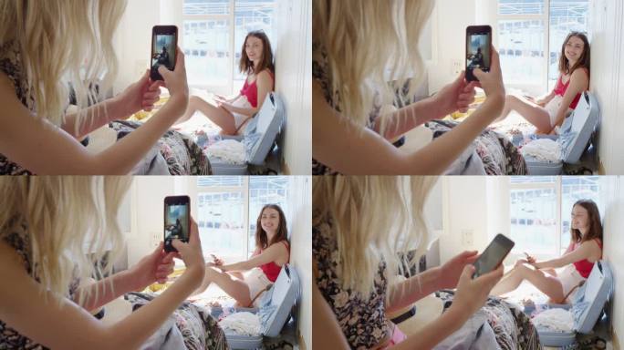 一名女子在酒店房间用智能手机拍下女友的照片，穿着夏日短裤，用手机技术分享欧洲度假的旅行照片