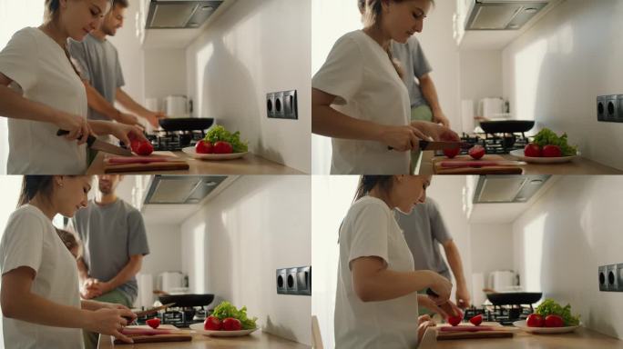 一个穿白色t恤的黑发女孩正在准备早餐沙拉，她的丈夫，一个穿灰色t恤的男人，和她说话，早上在厨房的炉子
