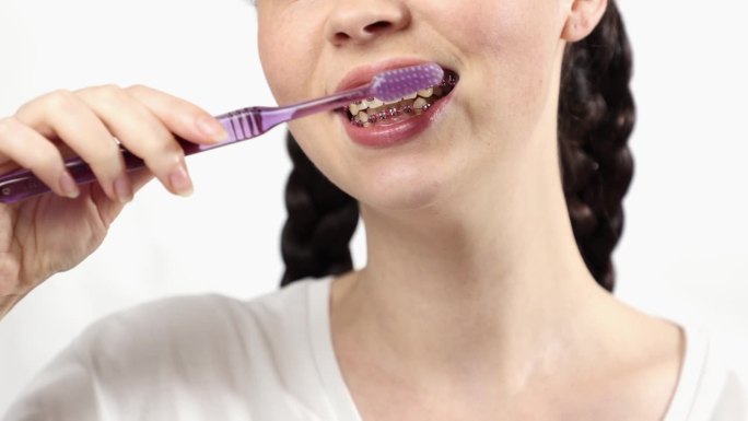 戴绑带牙套的年轻白人妇女用手动牙刷刷牙的特写。正畸治疗和牙齿护理的概念