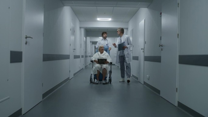 医生扶着轮椅上的老妇人走过医院走廊