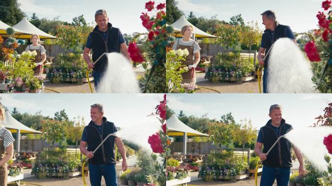 在花园中心，一名穿着围裙的妇女推着一手推车的植物在户外工作，而一名成熟的男子则用软管向植物喷水——慢