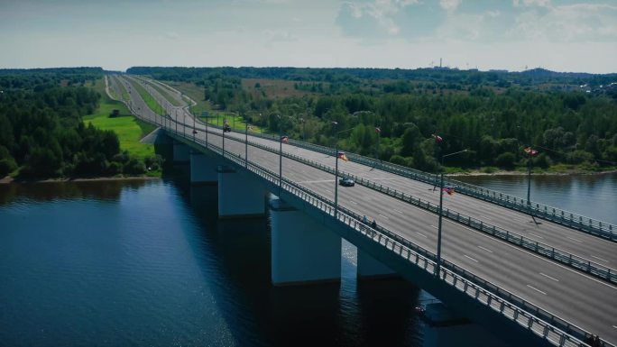 一条现代化的沥青高速公路蜿蜒而过，蜿蜒穿过绿色的草地和森林，横跨一座通往河流的桥。无人机拍摄的