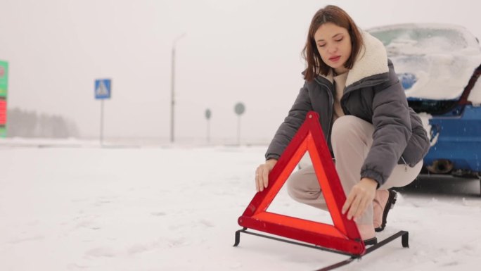 女人在冬天下雪的路上竖起了一个三角警示牌，汽车在冬天抛锚