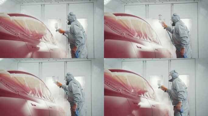 男喷漆技师在车身车间给汽车零件喷枪涂红漆。汽车服务站。工人在特殊车库为红色电动汽车喷漆，穿着工作服和