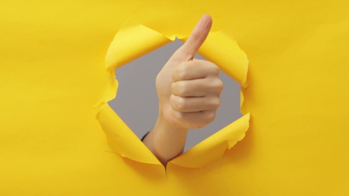 批准。做得很好。超级好。女性伸出大拇指在突破纸洞撕破墙纸在黄色复制空间背景。