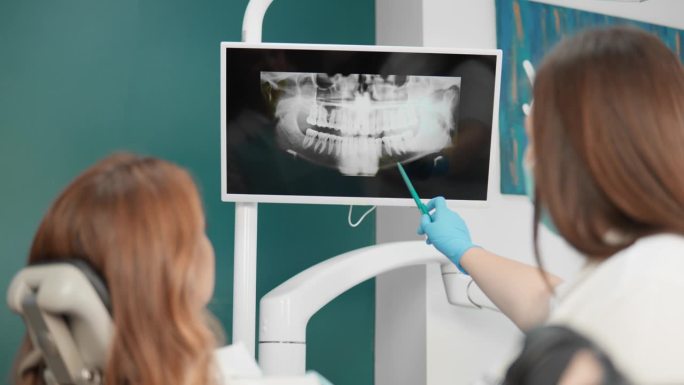 牙医给这位妇女看牙齿的x光片，作详细检查。牙医使用全景断层扫描来准确诊断口腔的问题。
