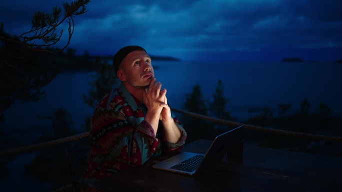 自由撰稿人或记者在晚上用笔记本电脑远程工作，男人看着打开的笔记本
