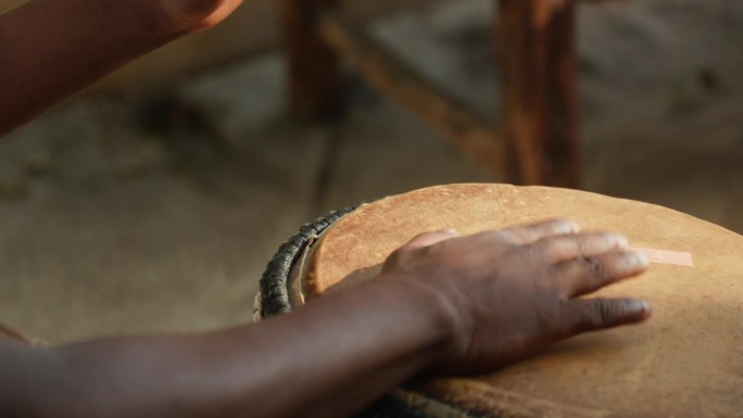 特写的非洲男子手打邦戈，突出修复鼓，背景是下午晚些时候美丽的灯光。