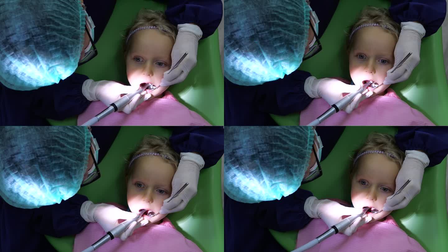 儿科牙医用牙钻和牙镜治疗龋齿。放大后的女孩张着嘴坐着，平静地等待着龋齿治疗的结束。概念治疗早期龋齿