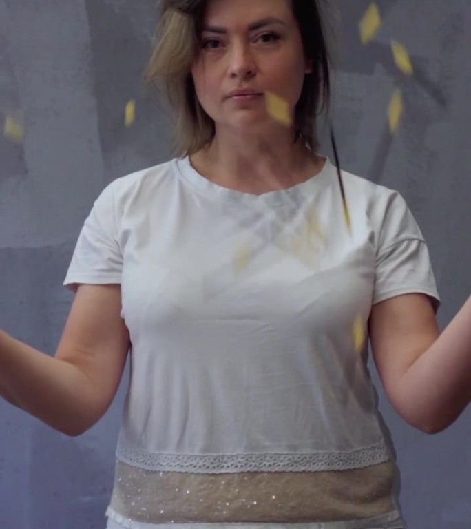 视频中，一个自信的女人站在灰色的背景下，朝前看，扔掉一次性睫毛刷。