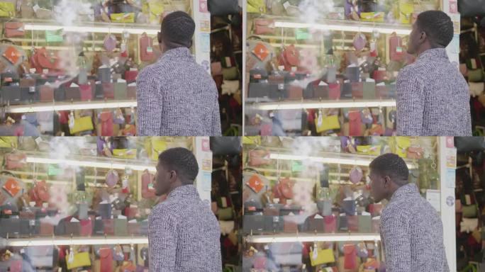 一名年轻的非洲男子站在一家皮具店的橱窗前，看着陈列的商品