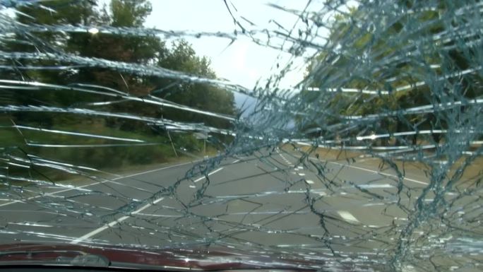 从一辆行驶在挡风玻璃破裂的道路上的汽车里看到的景象。4 k的视频。