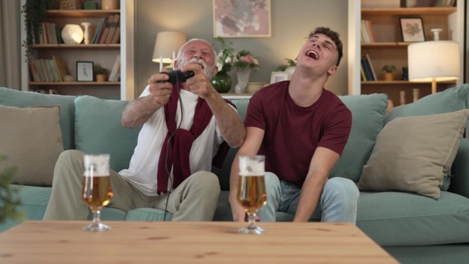 白人少年和老人爷爷和孙子坐在家里的沙发床上玩游戏机视频游戏拿着操纵杆控制器玩得很开心家庭纽带男性男性