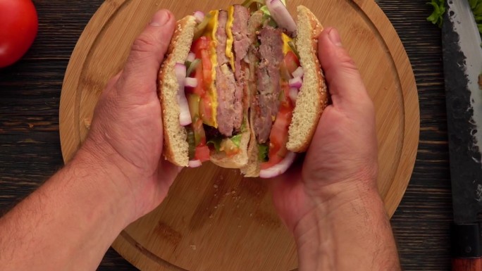 俯视图:男性双手张开的汉堡，肉排切成两半