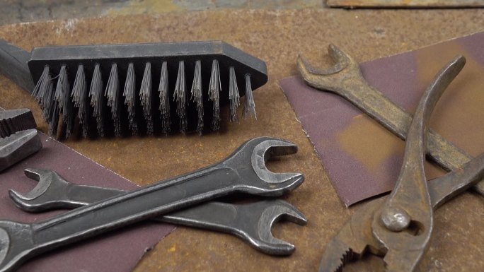 生锈的金属片上躺着工作和生锈的旧仪器、砂纸和钢丝刷。清理和修复旧仪器