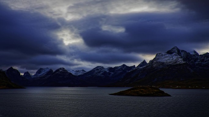 冷风吹过被白雪覆盖的群山环绕的挪威峡湾;乌云从右边进入画面。罗弗敦，挪威北部。