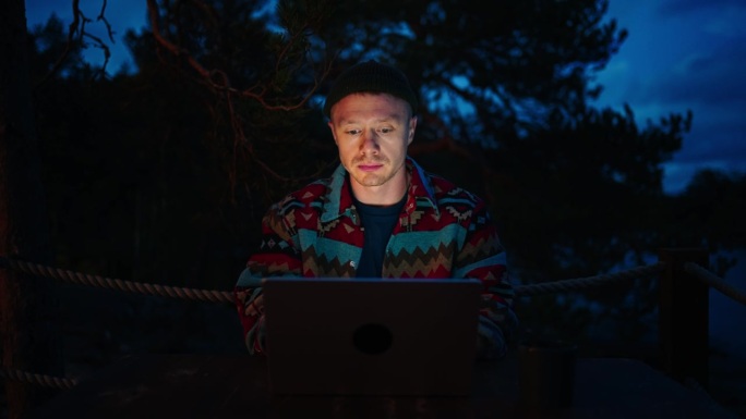 专业黑客在晚上用笔记本电脑工作，用笔记本照亮脸的人的肖像