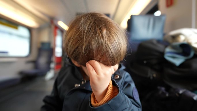 小孩乘火车时用手揉眼睛。小男孩挠脸治痒