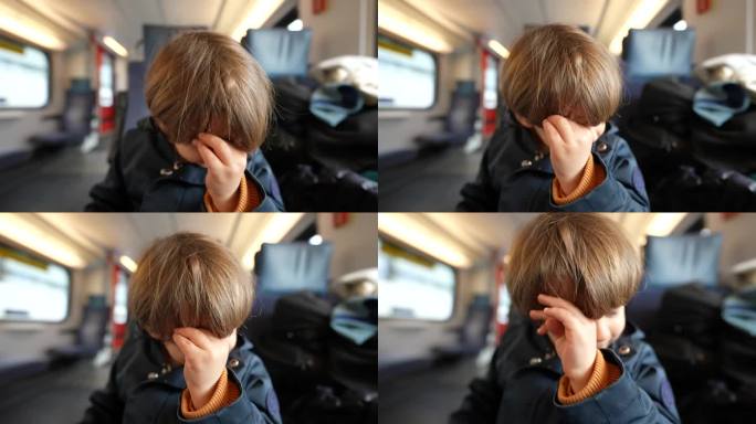 小孩乘火车时用手揉眼睛。小男孩挠脸治痒