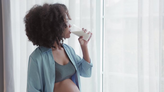 快乐的非洲孕妇喝着牛奶，抚摸着她的肚子
