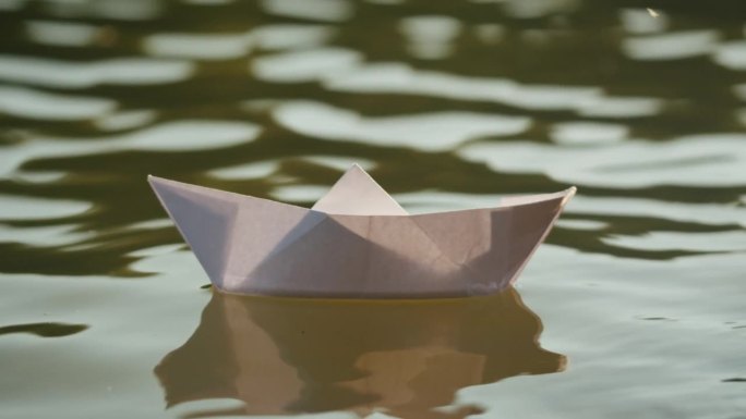 一个女人把纸船放在公园里的水上。池塘上的折纸鹤。晴天的自然湖景