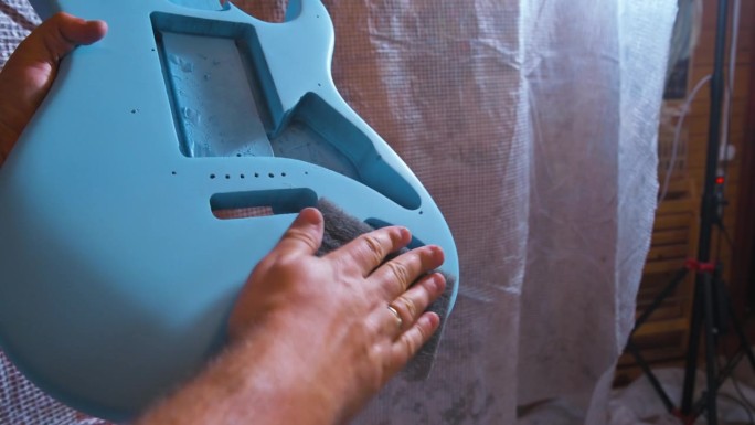 男子用蓝色喷雾罐喷涂电吉他本体。4k视频片段UHD 3840x2160