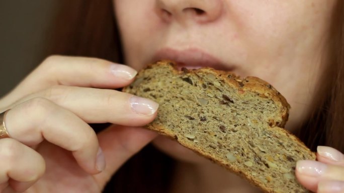 女人吃一片全麦面包。肖像特写。女人嘴里吃着硬皮面包
