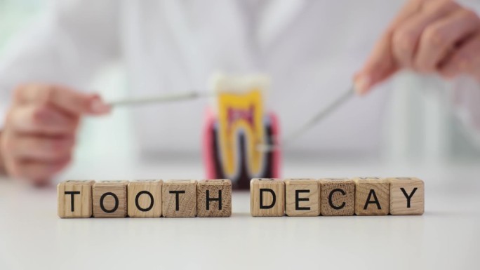 牙医展示人工牙和牙科器械，说明蛀牙