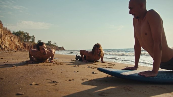 一个有经验的冲浪者，一个秃顶的男人，教他的学生如何在夏天在海边的沙滩上正确地游泳。陆上冲浪课