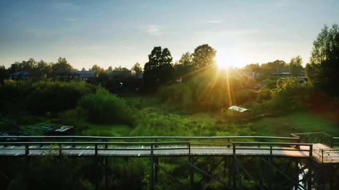 低洼地区的木桥。日落时的阳光，低矮的房屋，周围的绿色植物。俄罗斯省景观。无人机航拍