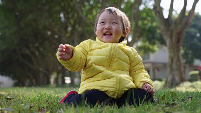 穿鸭黄羽绒服的小女孩坐在早春公园草地微笑