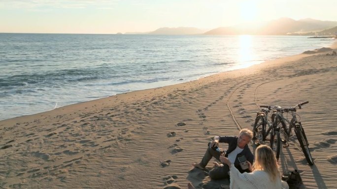 成熟的夫妇在空旷的海滩上喝着普罗塞克