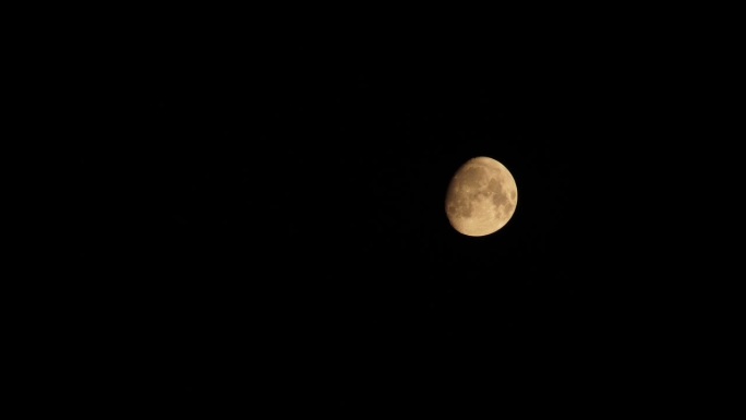 皎洁的月亮伴着云彩落下。半明半暗的月亮正在落下。黑色的云漂浮在带有陨石坑的黄色月亮的背景下。4k视频