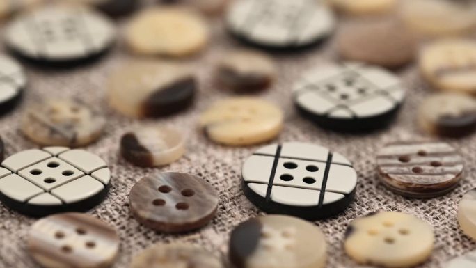 在粗麻布的织物背景上的棕色米色不同的按钮集。特写镜头旋转。