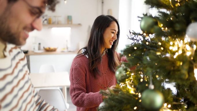 多种族夫妇，高加索男人和日本女人，在家里装饰圣诞树