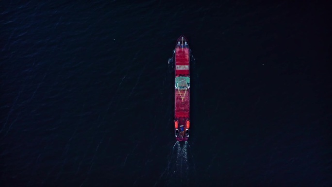 一艘夜间航行的干货船，船上有红色的甲板和橙色的救生艇。前视图。无人机航拍