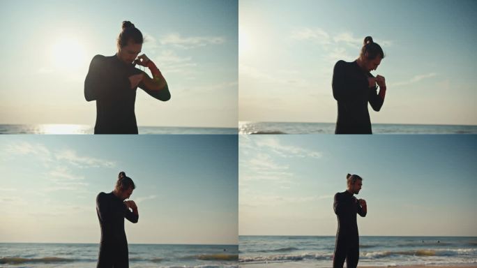 在一个阳光明媚的夏日，一名身穿黑色潜水服的黑发男子站在海边的沙滩上整理肩膀上的衣服。夏天，一名男子在