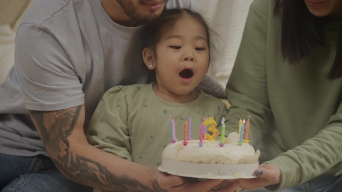 小女孩在生日蛋糕上吹蜡烛庆祝三岁生日