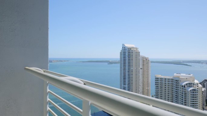 在晴朗的天空下，白色豪华摩天大楼和绿松石海洋的顶层阳台景色。新的高层公寓在现代住宅综合体揭示迷人的迈