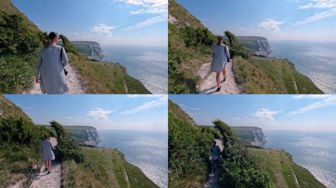 女游客带着相机沿着风景秀丽的海岸小径走在高高的悬崖上