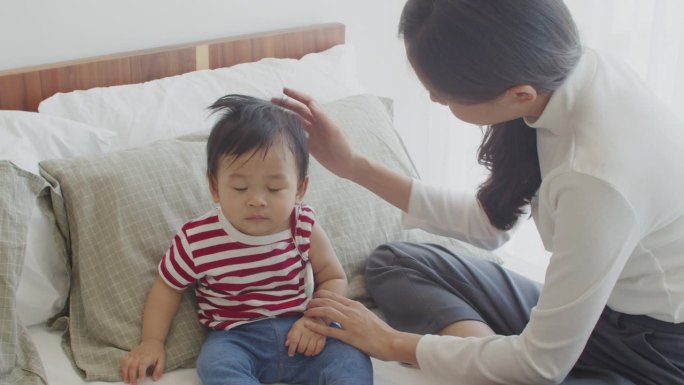 年轻的亚洲母亲在儿子患流行性感冒发烧时，小心使用电子体温计为他量体温。