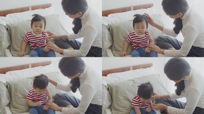 年轻的亚洲母亲在儿子患流行性感冒发烧时，小心使用电子体温计为他量体温。