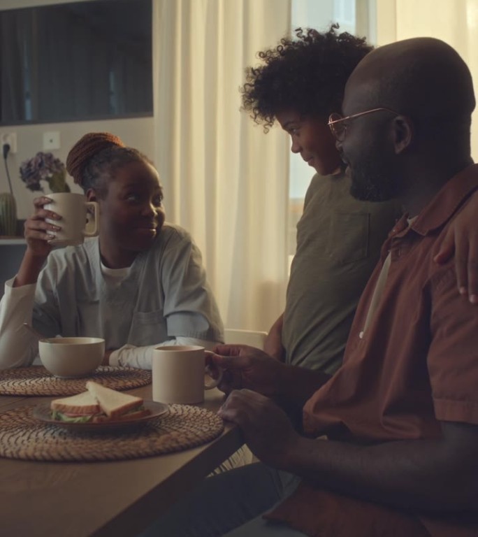 穿着护士服的黑人妇女在早餐时与丈夫和儿子聊天