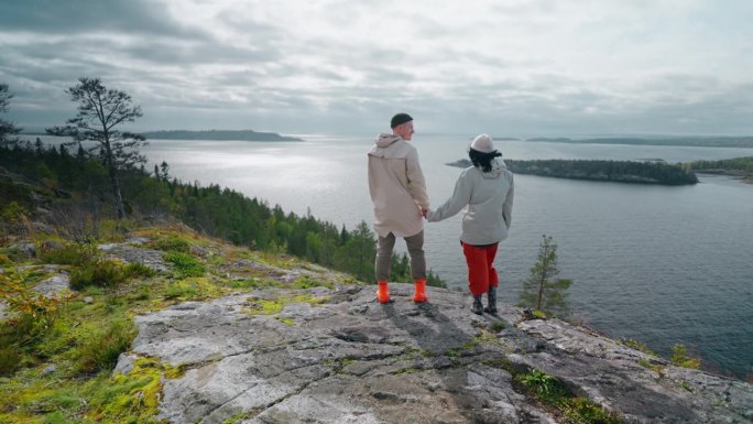 幸福的爱的男人和女人站在山顶和欣赏风景与峡湾，后视图