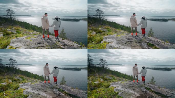 幸福的爱的男人和女人站在山顶和欣赏风景与峡湾，后视图