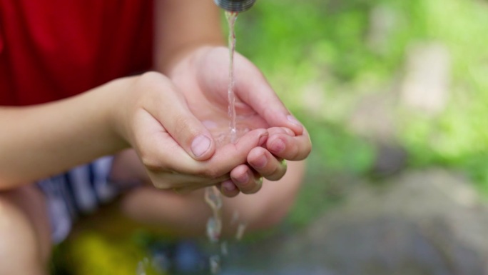 孩子的手从水龙头里接水，清澈的水从水龙头流入手中