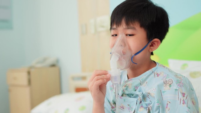 病童坐在病床上，在医院病房用雾化器吸入器管理哮喘。吸入器口罩强调了呼吸护理的重要性和医学专家在改善他