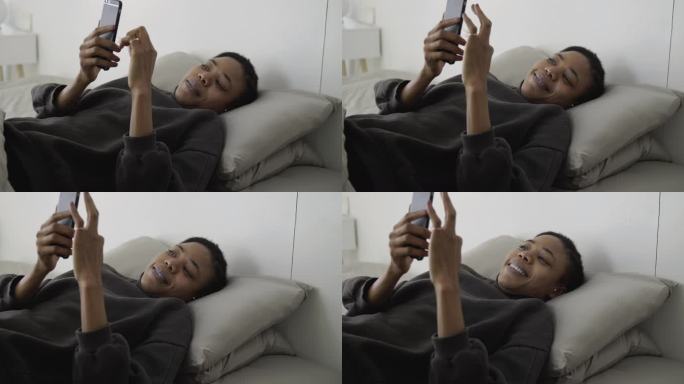 黑人美女躺在床上开心看手机