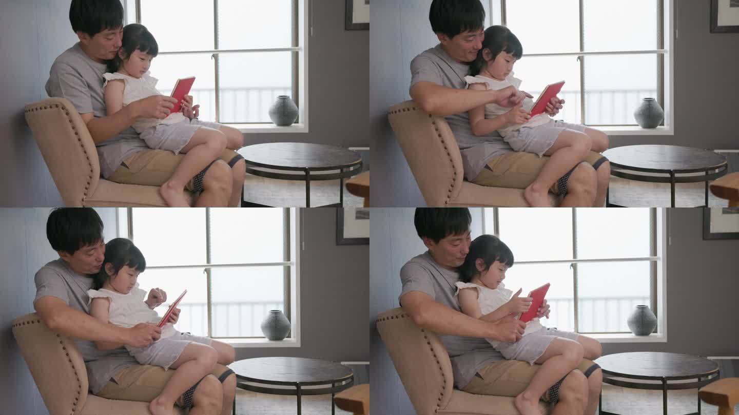一个女孩坐在她父亲的腿上操作平板电脑。