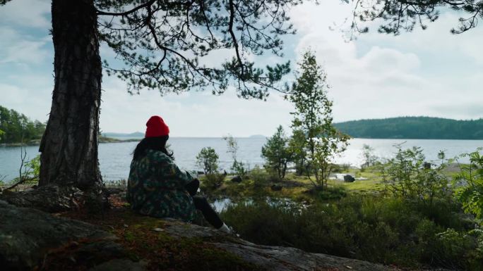 孤独的红帽女人独自在岩石上休息，看湖的风景，放松和冥想
